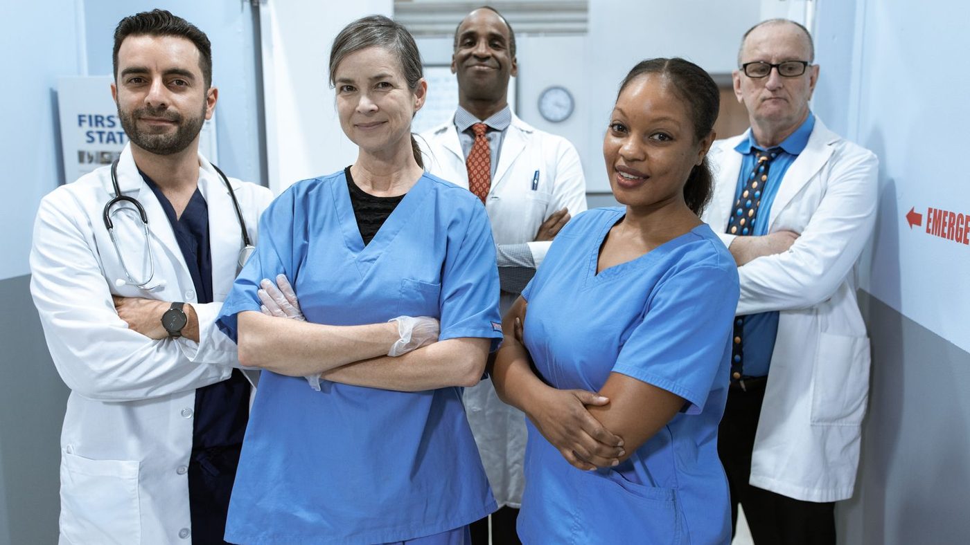A team of doctors and nurses in scrubs and white coats standing together in a hospital corridor